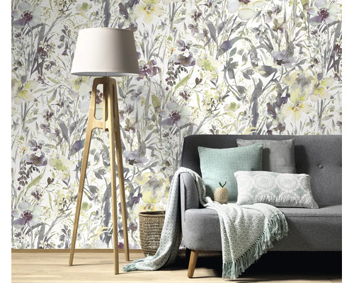 Woonkamer met vliesbehang met aquarel bloemenmotief achter een grijze bank met een statief vloerlamp op een houten vloer.