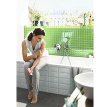 Vrouw zit op de rand van een bad in een moderne badkamer met groene mozaïektegels en een badmengkraan met handdouche.
