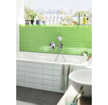 Moderne badkamer met een wit bad, kraan, groene mozaïektegels en een raam met uitzicht op de stad.
