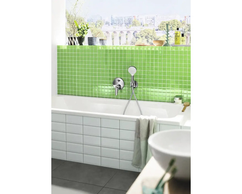 Moderne badkamer met een wit bad, kraan, groene mozaïektegels en een raam met uitzicht op de stad.