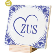 Vierkante tegel met decoratieve opdruk en de tekst ZUS, gepresenteerd op een houten houder.