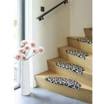 Houten trap met traptreden in luipaardprint, decoratieve vloervaas met kunstbloemen en zwarte trapleuning in de woonkamer.