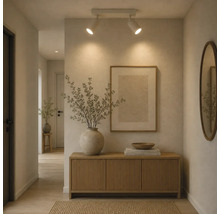 Een moderne hal met houten dressoir, ronde wandspiegel, ingelijste afbeelding en plafondspots die warm licht op de muur werpen.