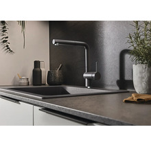 Moderne keukenkraan met uittrekbare sproeier bij een donkere spoelbak in een stijlvolle keuken met donkere achterwand.