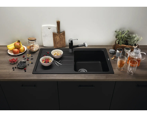 Moderne zwarte inbouwspoelbak met afdruiprek en bijpassende kraan in een keuken met houtlook werkblad en donkere keukenkastjes.