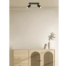 Tweevoudige plafondspot van metaal aan het plafond boven een dressoir met rotan elementen in een modern ingerichte ruimte.