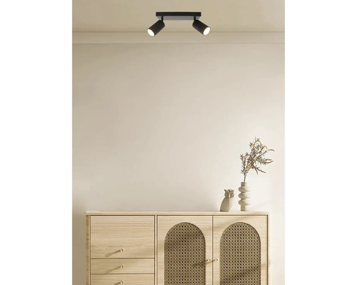 Tweevoudige plafondspot van metaal aan het plafond boven een dressoir met rotan elementen in een modern ingerichte ruimte.