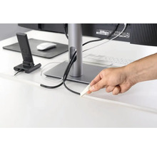 Hand plaatst een zelfklevende kabelgoot op een bureau voor het netjes wegwerken van kabels bij de computerwerkplek.