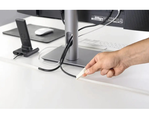 Hand plaatst een zelfklevende kabelgoot op een bureau voor het netjes wegwerken van kabels bij de computerwerkplek.