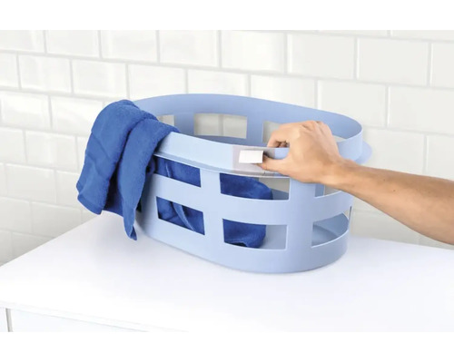 Ovale kunststof wasmand met handgrepen en ventilatieopeningen gevuld met een handdoek op een plank.