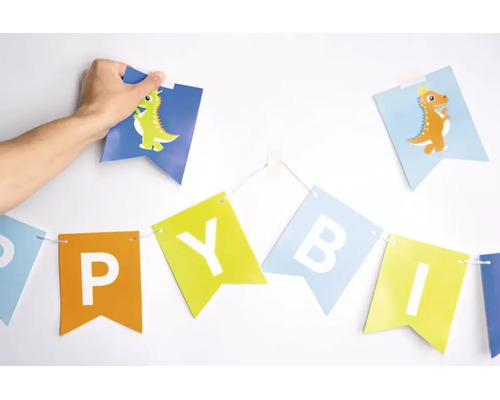 Een hand bevestigt een slinger met dinosaurusafbeeldingen en letters aan een muur ter decoratie.
