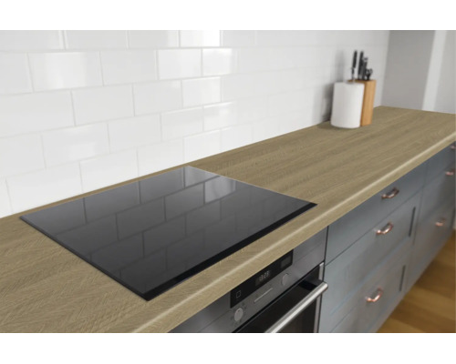 Moderne keukenopstelling met houtstructuur werkblad, inductiekookplaat, oven en witte wandtegels.