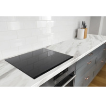 Moderne keukenopstelling met witte tegels, marmerlook werkblad, zwarte kookplaat en daaronder een oven met digitaal display.