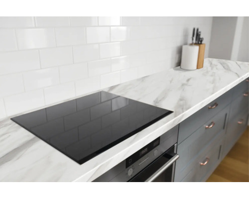 Moderne keukenopstelling met witte tegels, marmerlook werkblad, zwarte kookplaat en daaronder een oven met digitaal display.