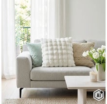 Een lichte woonkamer met een bank versierd met drie verschillende sierkussens en een salontafel met een vaas vol bloemen. (Image AI modified or generated)