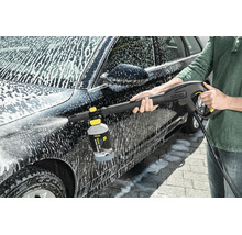 Persoon reinigt een auto met een Kärcher hogedrukreiniger en een schuimsproeier met reinigingsmiddel.