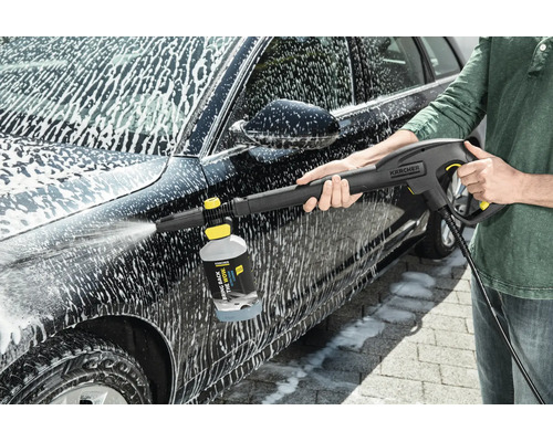 Persoon reinigt een auto met een Kärcher hogedrukreiniger en een schuimsproeier met reinigingsmiddel.