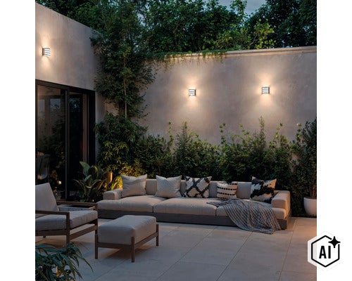 Moderne buitenwandlampen gemonteerd aan een tuinmuur boven een gezellige zithoek met bank en fauteuil in de avond. (Image AI modified or generated)