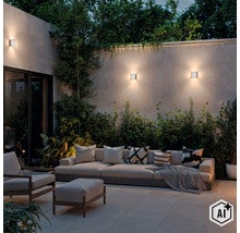 Moderne buitenwandlampen gemonteerd aan een tuinmuur boven een gezellige zithoek met bank en fauteuil in de avond. (Image AI modified or generated)