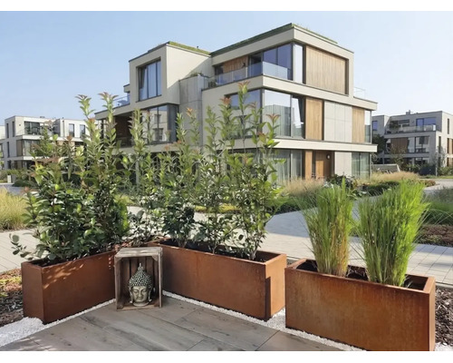 Moderne tuinterras met plantenbakken van cortenstaal en een Boeddhabeeld voor een appartementencomplex met houten elementen.
