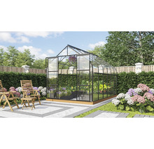 Vrijstaande kas met glazen wanden en metalen frame in een verzorgde tuin met houten stoelen op een terras.