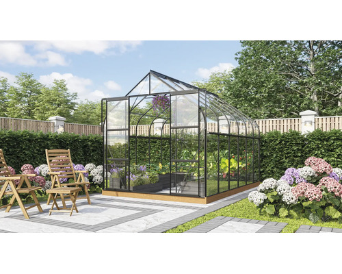 Vrijstaande kas met glazen wanden en metalen frame in een verzorgde tuin met houten stoelen op een terras.