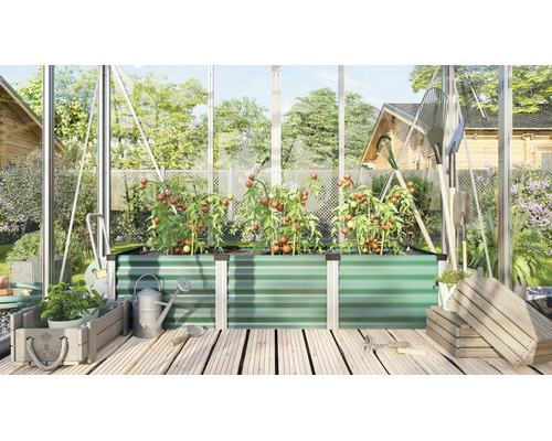 Een verhoogde plantenbak van geprofileerd metaal in een kas met tomatenplanten, tuingereedschap en houten kisten op een houten terrasvloer.