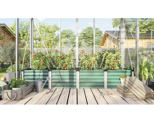 Een verhoogde plantenbak van metaal in een kas, beplant met tomaten, omringd door tuingereedschap en houten kisten op een houten vloer.