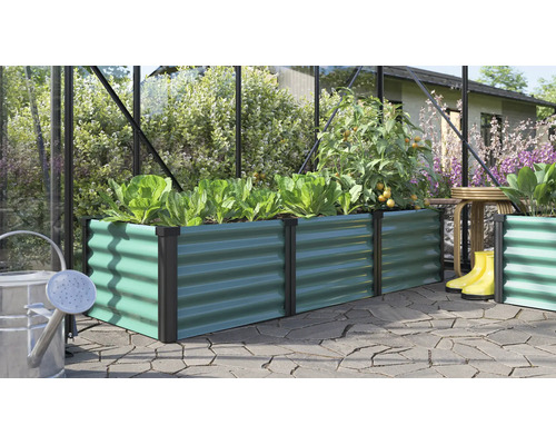 Rechthoekige verhoogde plantenbak van metaal met golfstructuur in een kas met planten en tuingereedschap op een terras.