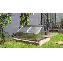 Een koude bak met aluminium frame en kanaalplaten in een tuin op een gemetselde rand voor een huismuur.