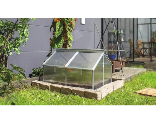 Een koude bak met aluminium frame en kanaalplaten in een tuin op een gemetselde rand voor een huismuur.