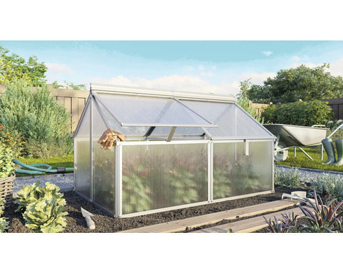 Aluminium broeibak met kanaalplaten in een zonnige tuin met tuingereedschap en planten op de achtergrond.
