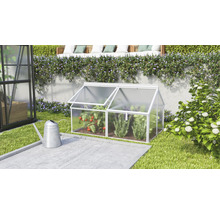 Een kleine koude bak van aluminium en kanaalplaten in de tuin naast een gieter met twee openklapbare dakramen voor het kweken van planten.