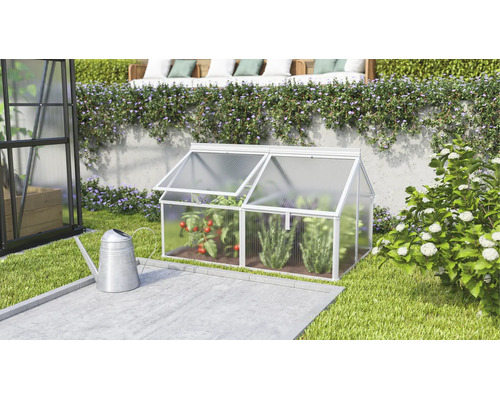 Een kleine koude bak van aluminium en kanaalplaten in de tuin naast een gieter met twee openklapbare dakramen voor het kweken van planten.