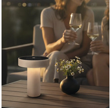 Moderne solartafellamp met geïntegreerd zonnepaneel op een terrastafel naast een bloemenvaas bij twee personen met wijnglazen.