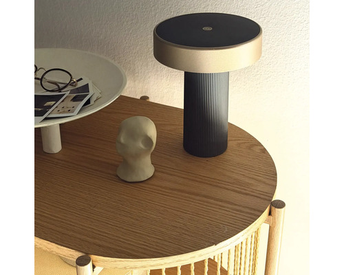 Moderne oplaadbare lamp op een ronde houten bijzettafel met decoratieve objecten.