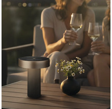 Moderne LED tafellamp voor buiten met zonnepaneel op een tuintafel naast een bloemenvaas en twee personen.