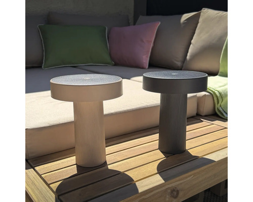 Twee ronde, moderne LED tafellampen met geribbelde voet op een houten terras voor een loungebank.