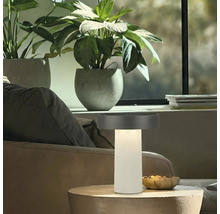 Moderne led tafellamp met geribbelde zuilvoet en platte kap op een houten tafel in een lichte woonkamer.