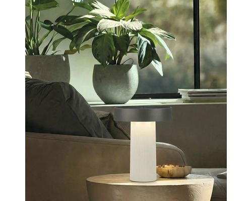 Moderne led tafellamp met geribbelde zuilvoet en platte kap op een houten tafel in een lichte woonkamer.