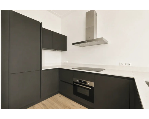 Moderne L-vormige inbouwkeuken met donkere fronten, wit werkblad, inductiekookplaat, ingebouwde oven en afzuigkap.