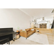 Open woonruimte met lederen bank, piano en verhoogd keukengedeelte met kookeiland in een modern en licht interieur.