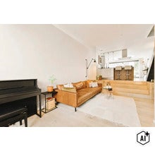Open woonruimte met lederen bank, piano en verhoogd keukengedeelte met kookeiland in een modern en licht interieur. (Image AI modified or generated)
