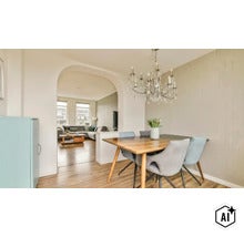 Eetkamer met houten tafel en gestoffeerde stoelen onder een kroonluchter, verbonden door een boog met een aangrenzende woonkamer. (Image AI modified or generated)