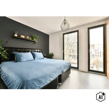 Moderne slaapkamer met tweepersoonsbed, donkere accentmuur, wandplank, hanglamp en grote ramen met daglicht. (Image AI modified or generated)