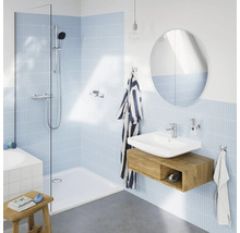 Moderne badkamer met inloopdouche, wastafel met houten onderkast, ronde spiegel en lichtblauwe tegels in een lichte ruimte.