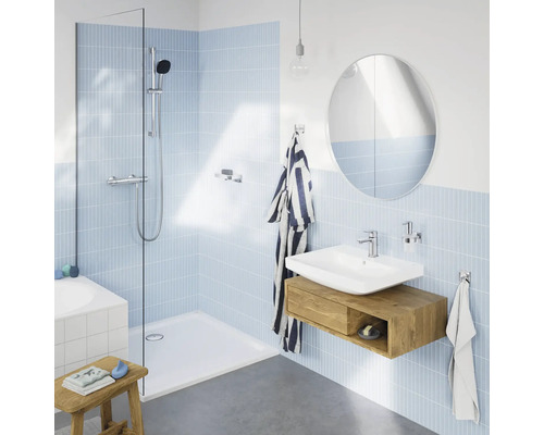 Moderne badkamer met inloopdouche, wastafel met houten onderkast, ronde spiegel en lichtblauwe tegels in een lichte ruimte.