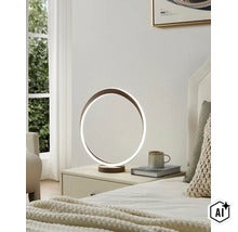 Moderne ringvormige LED tafellamp op een nachtkastje in de slaapkamer naast een boek en een mok. (Image AI modified or generated)