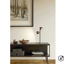 Moderne tafellamp met twee verstelbare spots op een dressoir voor een muur met schilderij en decoratieve objecten. (Image AI modified or generated)
