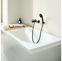 Moderne ligbad met badkraan en handdouche in een lichte badkamer, aangevuld met een houten badplank met accessoires.